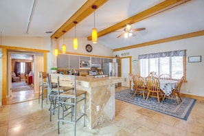 A spacious kitchen with a central island, wooden chairs, a dining table, and pendant lights.