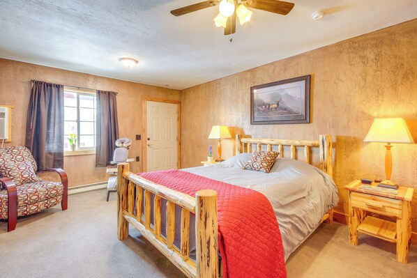 A bedroom with a wooden bed, a chair, a bedside table, and a ceiling fan. - Emigrant Lodge w/ Spa: 3 Suites Near Yellowstone (Emigrant)