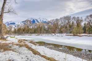 A snow-covered landscape with mountains in the background, a frozen pond, and a green chair. - Emigrant Lodge w/ Spa: 3 Suites Near Yellowstone (Emigrant)