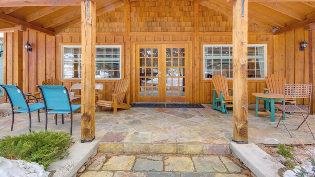 A wooden cabin with a stone patio, wooden chairs, and a wooden table. - Emigrant Lodge w/ Spa: 3 Suites Near Yellowstone (Emigrant)