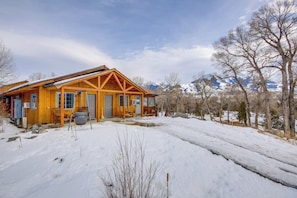 A wooden cabin with a porch, a garage, and a snow-covered landscape.