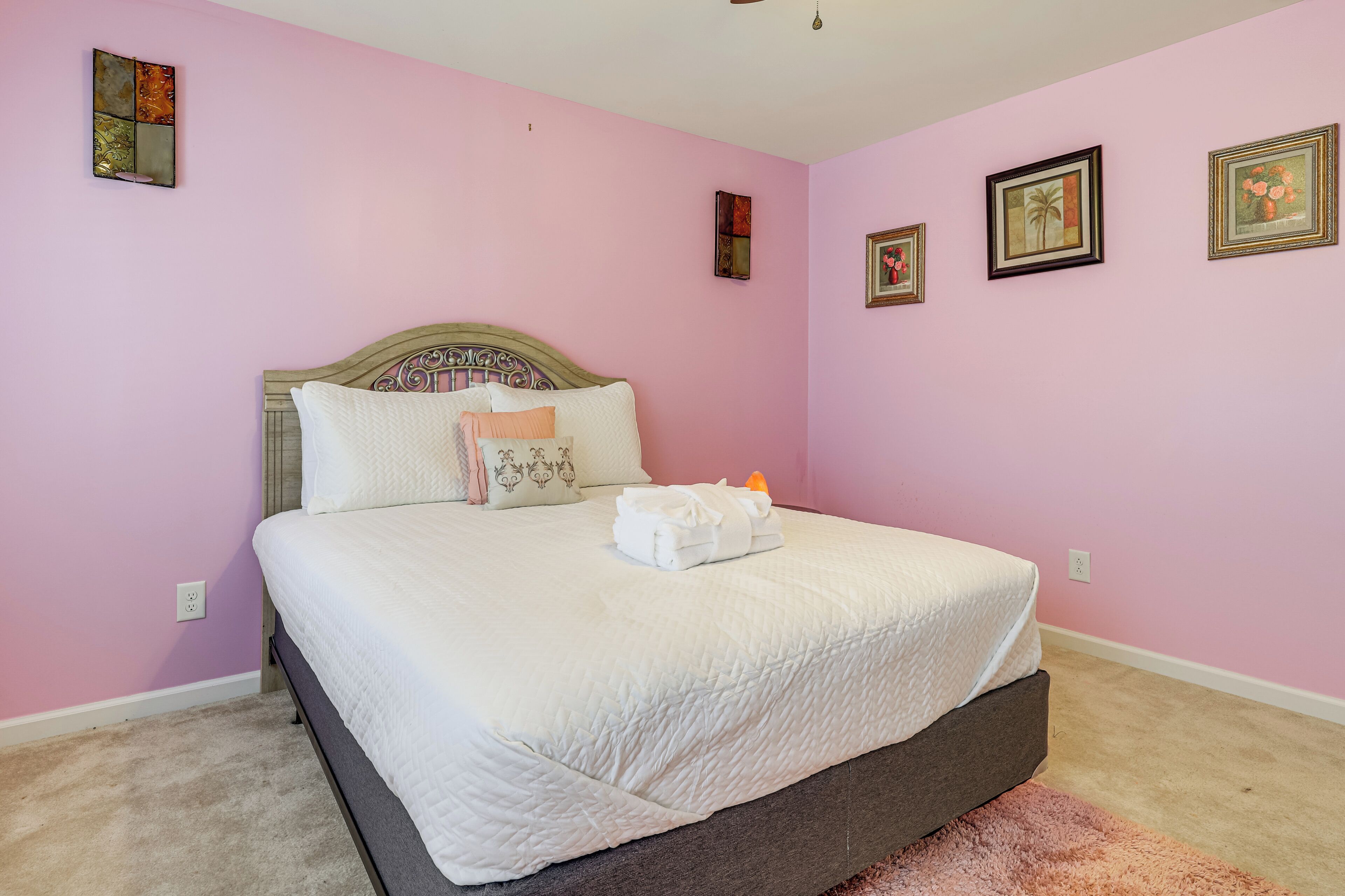 A bedroom with a bed, pink walls, and framed pictures.