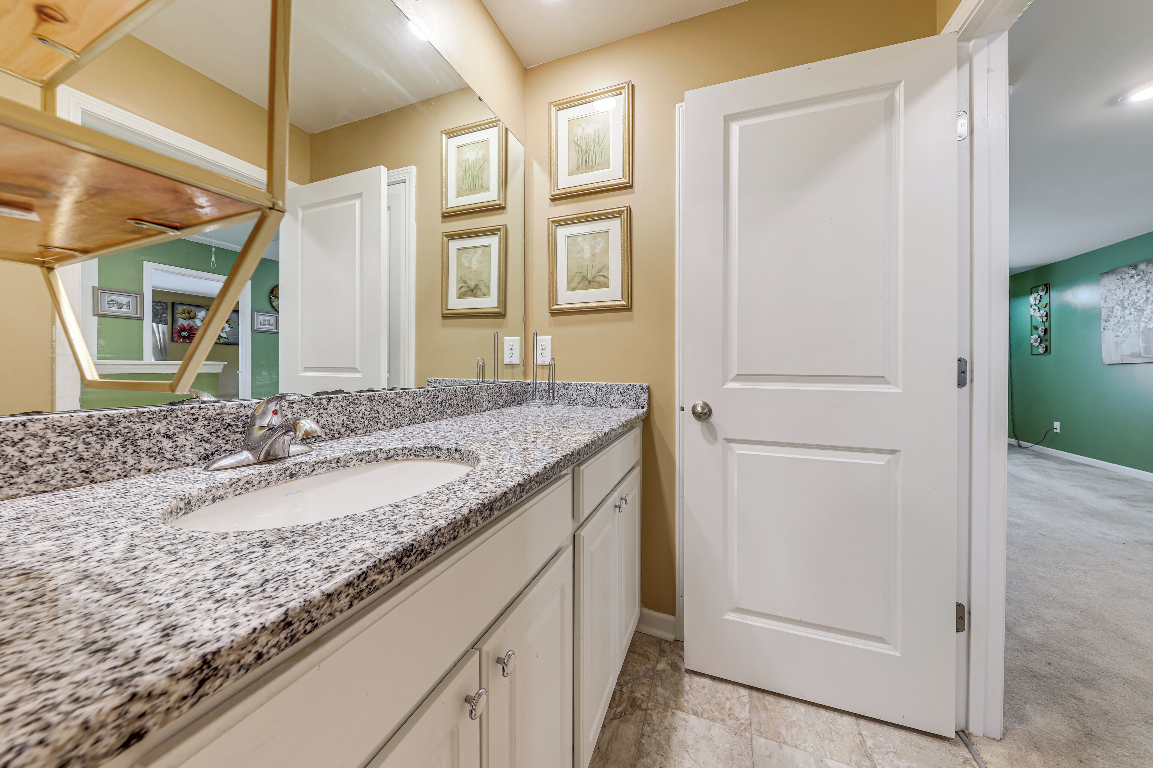 Une salle de bain avec un lavabo surmonté d’un plan de travail en granit, des meubles blancs et une porte blanche.