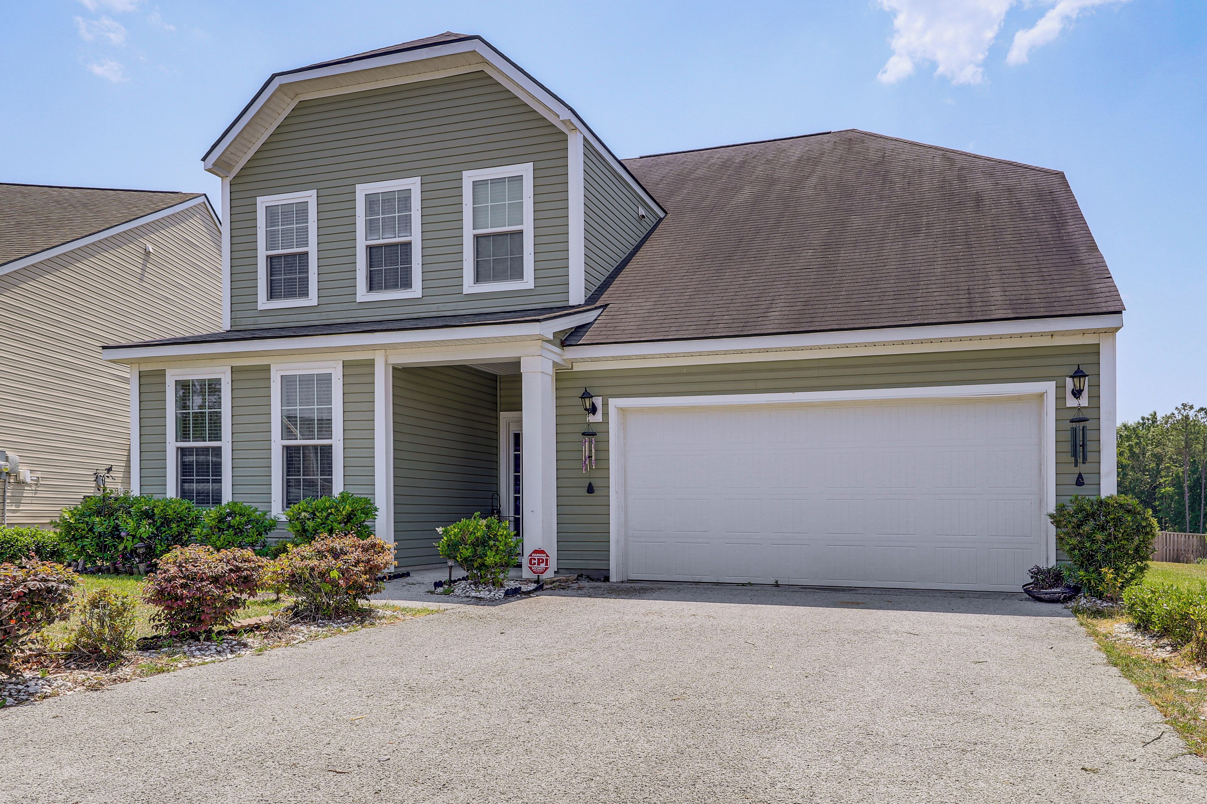 A two-story house with a garage, a covered porch, and a gravel driveway.