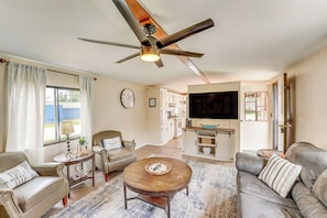 A living room with a ceiling fan, a coffee table, a sofa, a TV, and a kitchen area in the background. - Walk to Silver Lake State Park! Family Getaway (Mears)