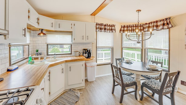 Une cuisine avec des armoires blanches, un plan de travail en bois, une cuisinière à gaz, un évier et un coin repas avec une table et des chaises.