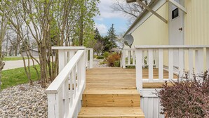 Une terrasse en bois menant à un bâtiment doté d’une balustrade blanche, d’une antenne parabolique et d’une porte.