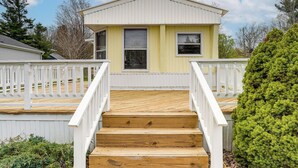 Une maison à deux étages avec une terrasse en bois, des rampes blanches et un arbuste vert.