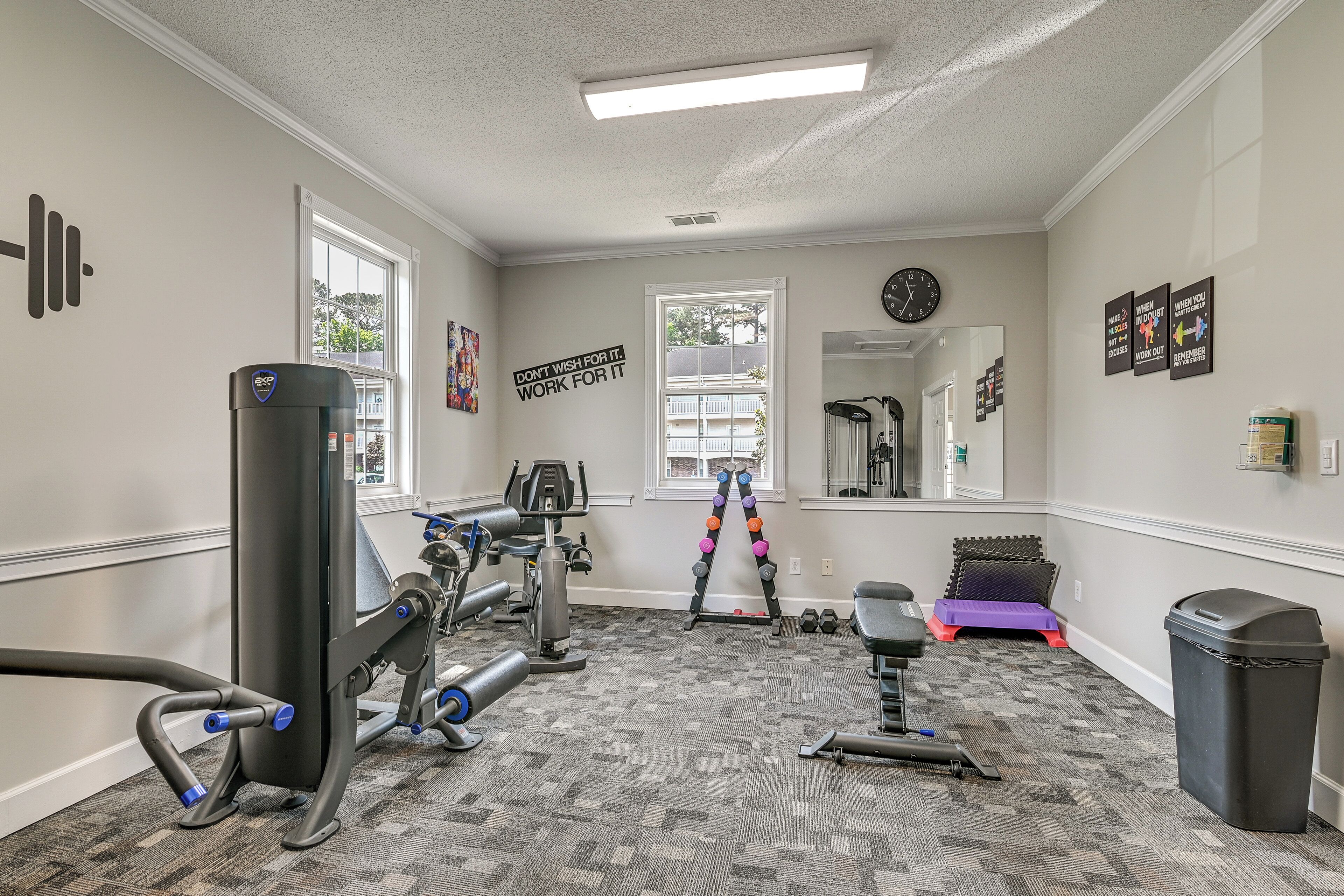 Ein Heimfitnessraum mit Trainingsgeräten, einem Fenster, einem Spiegel und motivierenden Wandbildern.