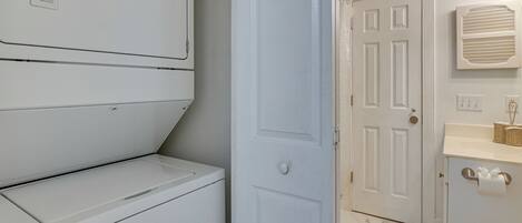 A laundry room with stacked washers and dryers, a white door, and a bathroom with a toilet, sink, and towel rack.