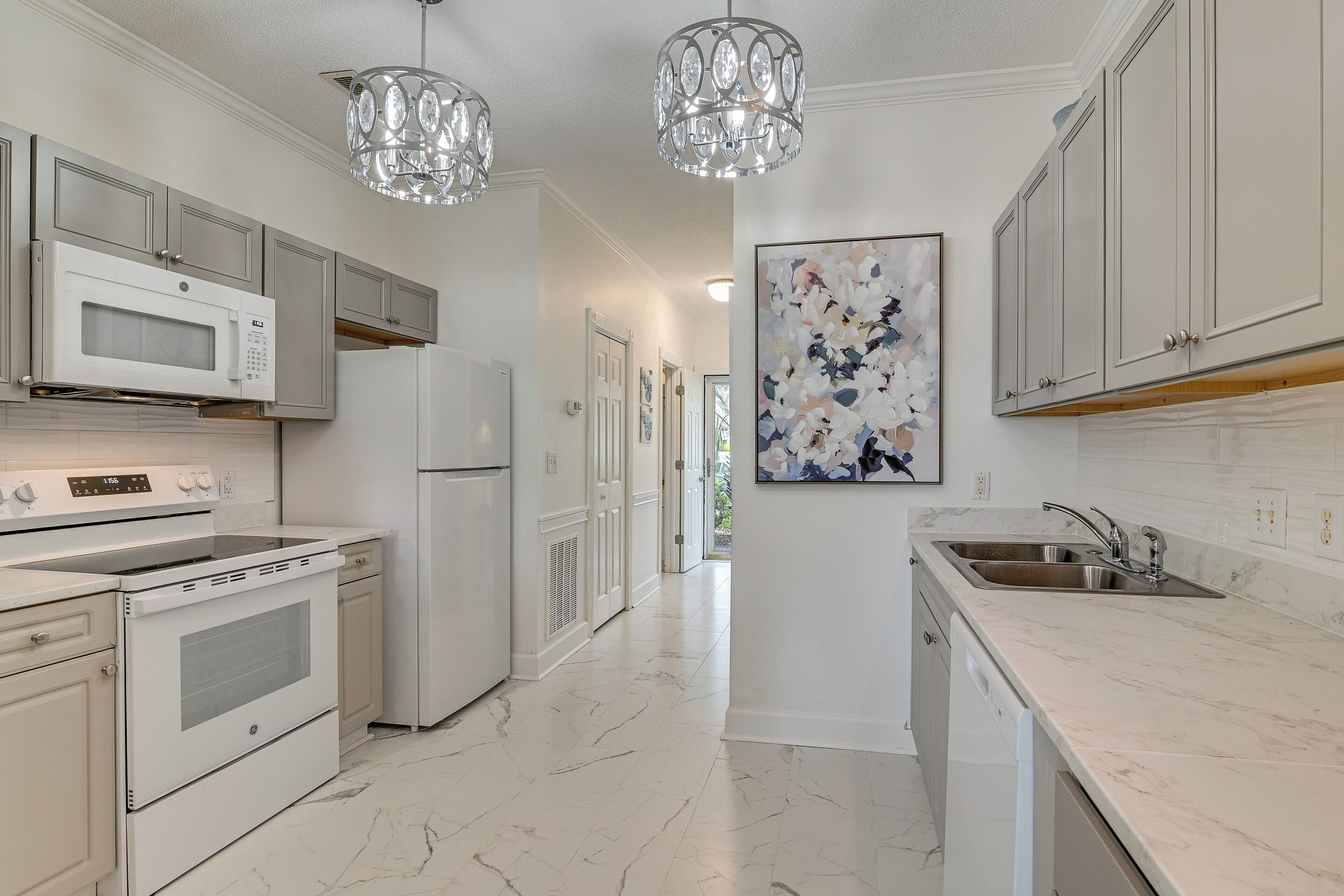 A modern kitchen with white cabinetry, a stainless steel sink, a microwave, an oven, and a refrigerator.