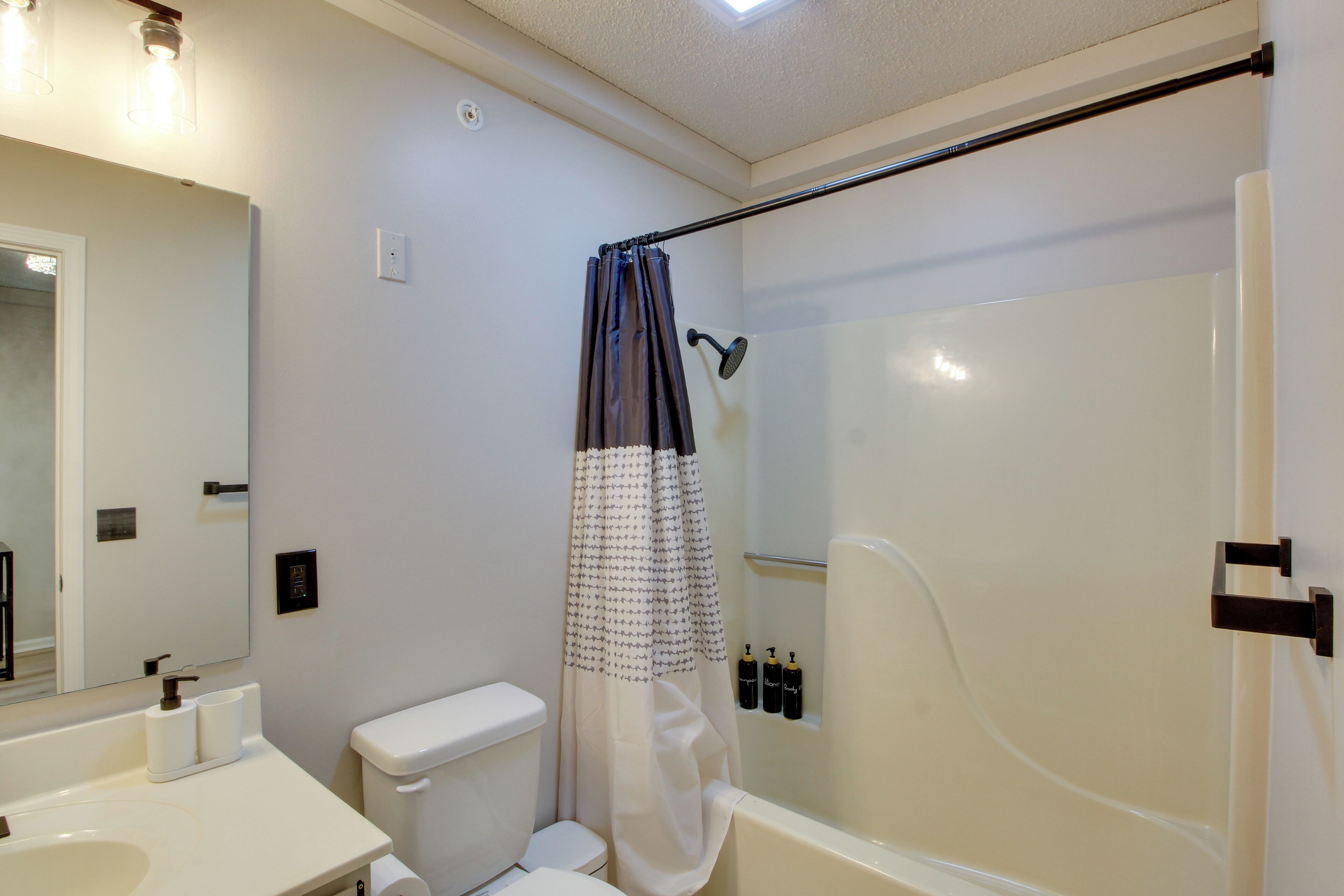 A bathroom with a toilet, sink, shower, and a mirror.
