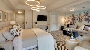 Una habitación de hotel moderna con cama, sofá, mesa de centro, televisor y un mural de palmeras.