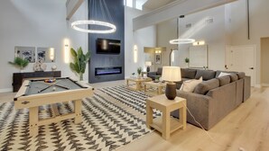 Una sala de estar moderna con una mesa de billar, un sofá, un televisor y una chimenea.
