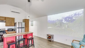 Una cocina moderna con barra, armarios de madera y una gran pantalla de proyección que muestra un paisaje montañoso.
