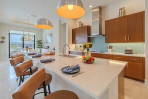 Une cuisine moderne avec des meubles en bois, un îlot central doté de sièges, un éclairage suspendu et une vue sur l’extérieur.