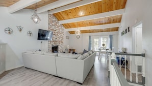 A modern living room with a sectional sofa, a TV, a fireplace, and a staircase leading to another level. - Gateway to Big Bear! High-country Home w/ Deck (Running Springs)