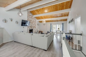 A modern living room with a sectional sofa, a TV, a fireplace, and a staircase leading to another level. - Gateway to Big Bear! High-country Home w/ Deck (Running Springs)