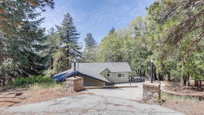 A house with a garage, surrounded by trees, and a driveway leading to the entrance. - Gateway to Big Bear! High-country Home w/ Deck (Running Springs)