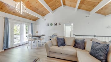 A spacious living area with a wooden ceiling, a beige sofa, and a dining table with chairs.