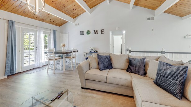 A spacious living area with a wooden ceiling, a beige sofa, and a dining table with chairs. - Gateway to Big Bear! High-country Home w/ Deck (Running Springs)