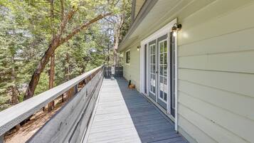 A wooden deck with a railing, a building with a white exterior, and trees in the background.