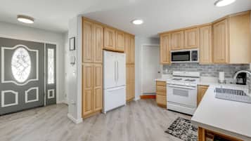 A modern kitchen with wooden cabinets, a refrigerator, a microwave, an oven, and a white countertop.