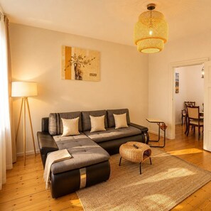 Una sala de estar con sofá, reposapiés, lámpara de pie y lámpara colgante.