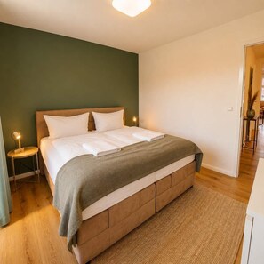 A bedroom with a bed, bedside tables, a nightstand, and a door leading to another room. - Spacious Maisonette in the Heart of Wismar (Wismar)