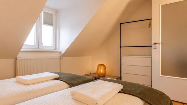 A bedroom with two beds, a window, a radiator, a bedside table with a lamp, and a wardrobe. - Spacious Maisonette in the Heart of Wismar (Wismar)