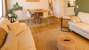 A modern living room with a sofa, dining table, and chairs, a kitchen in the background, and a large woven light fixture. - Spacious Maisonette in the Heart of Wismar (Wismar)