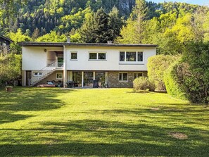 Ein zweistöckiges Haus mit einer überdachten Terrasse, einer Treppe und einem gepflegten Rasen.