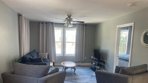 A living room with two armchairs, a coffee table, a ceiling fan, and a TV on a stand.