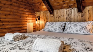 Een houten blokhut van binnen, met een bed, kussens en een wandlamp.