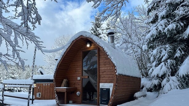 Een houten hut met een schuin dak, schoorsteen en een klein terras.