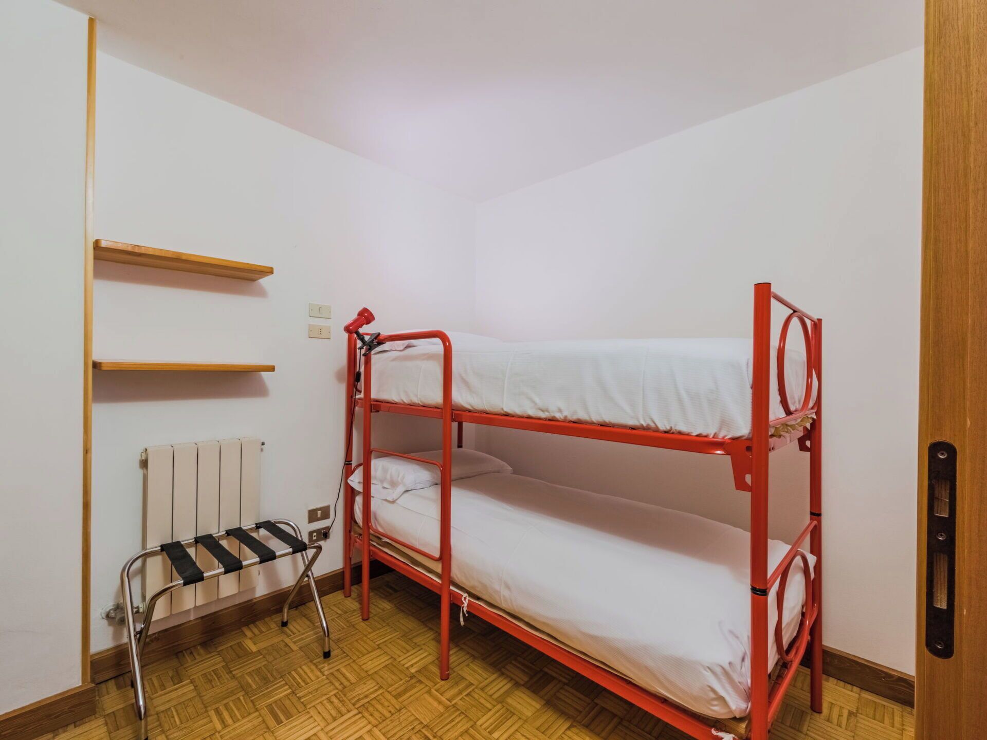 Dormitorio con literas, un radiador, una estantería pequeña y una silla.