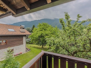 Ein Holzbalkon mit Blick auf eine Berglandschaft und ein Haus mit Ziegeldach.