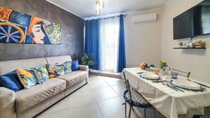 Ein Wohnzimmer mit einer Couch, einem Esstisch und einem an der Wand befestigten Fernseher.