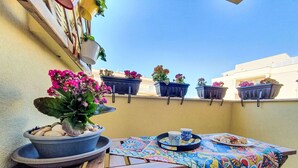 Eine Terrasse mit Tisch, Topfpflanzen und einer bunten Tischdecke.