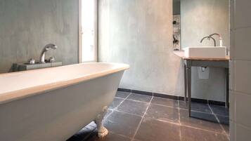 Un baño moderno con una bañera independiente, un lavabo con un grifo moderno y un suelo de baldosas.