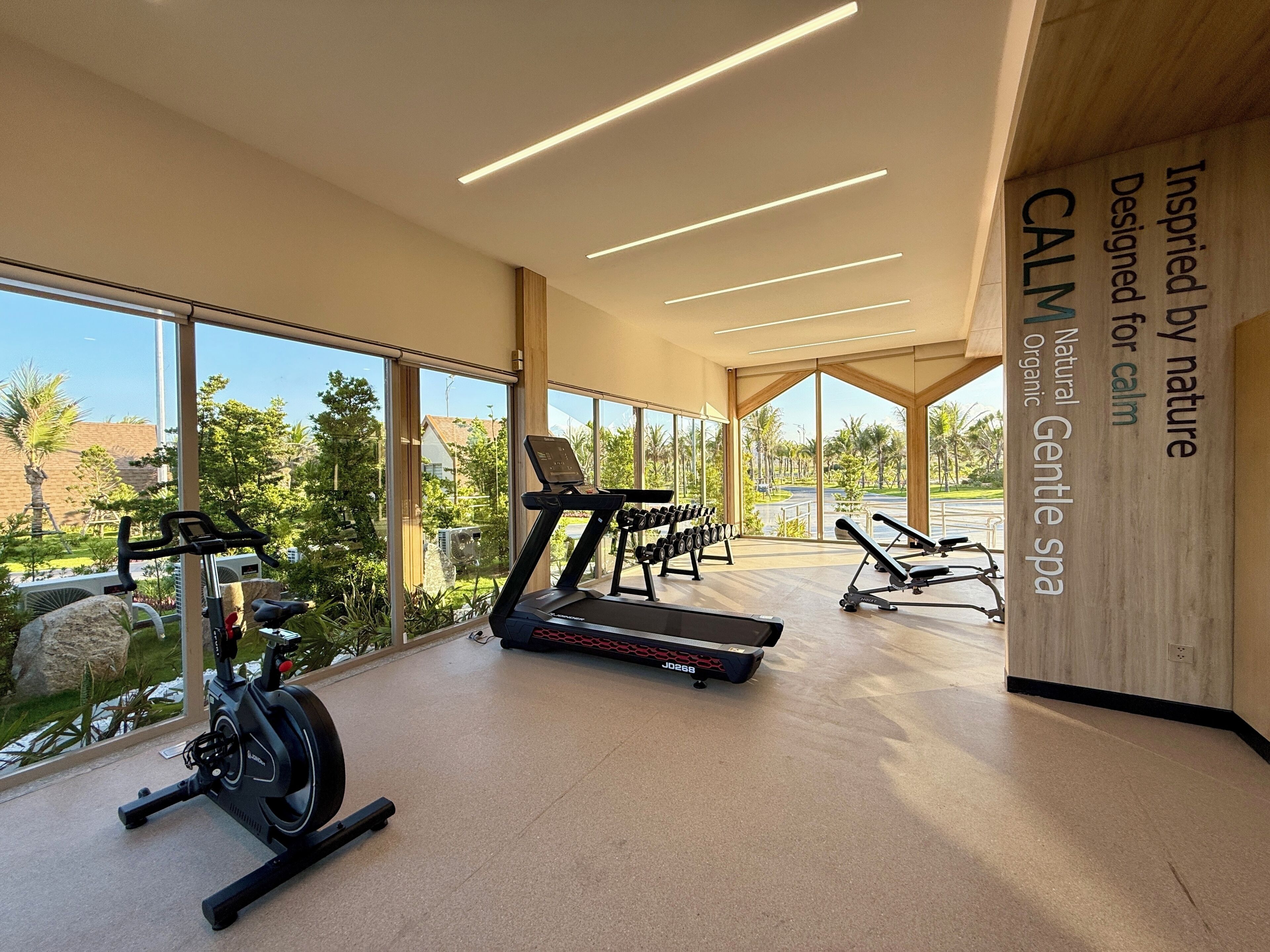 A gym with exercise equipment, large windows, and a sign reading 'Inspired by nature Designed for calm'.