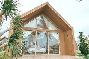 A modern house with a large glass door, a wooden deck, and a bed visible inside. - Carabeach Retreat (Cam Ranh)