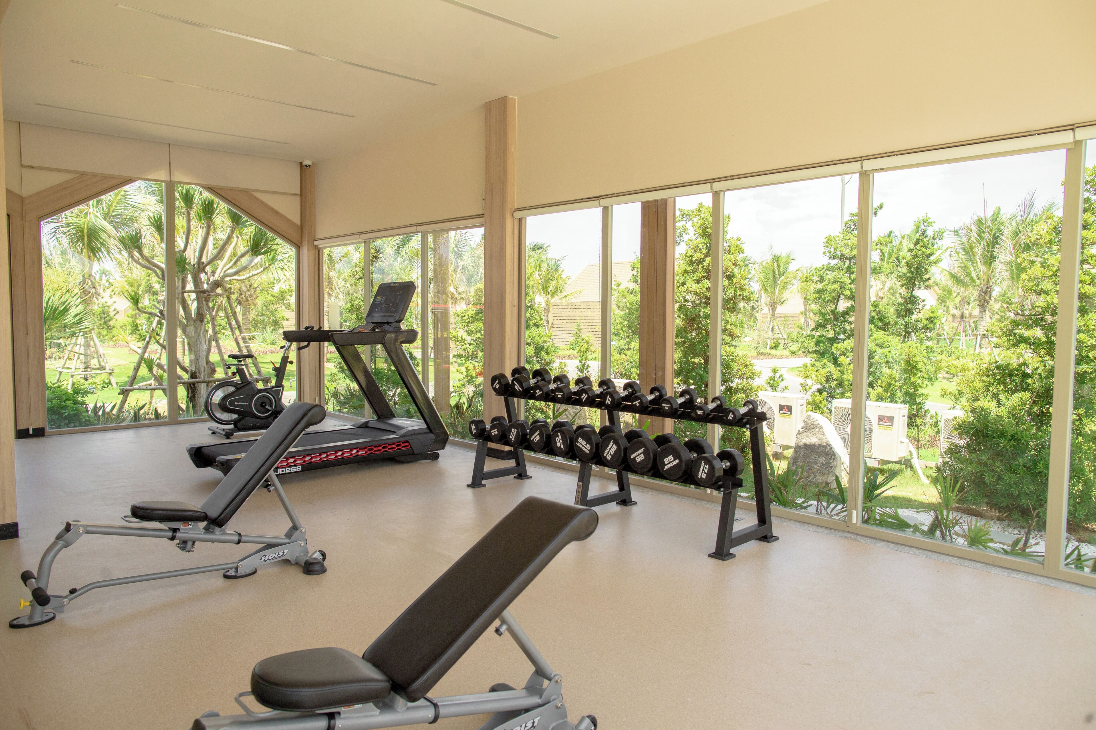 A gym with exercise equipment, large windows, and a view of greenery.