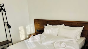 A neatly made bed with white linens, a wooden headboard, and a wooden floor.