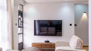 A modern living room with a flat-screen TV, beige sofas, a wooden coffee table, and a ceiling with recessed lighting.