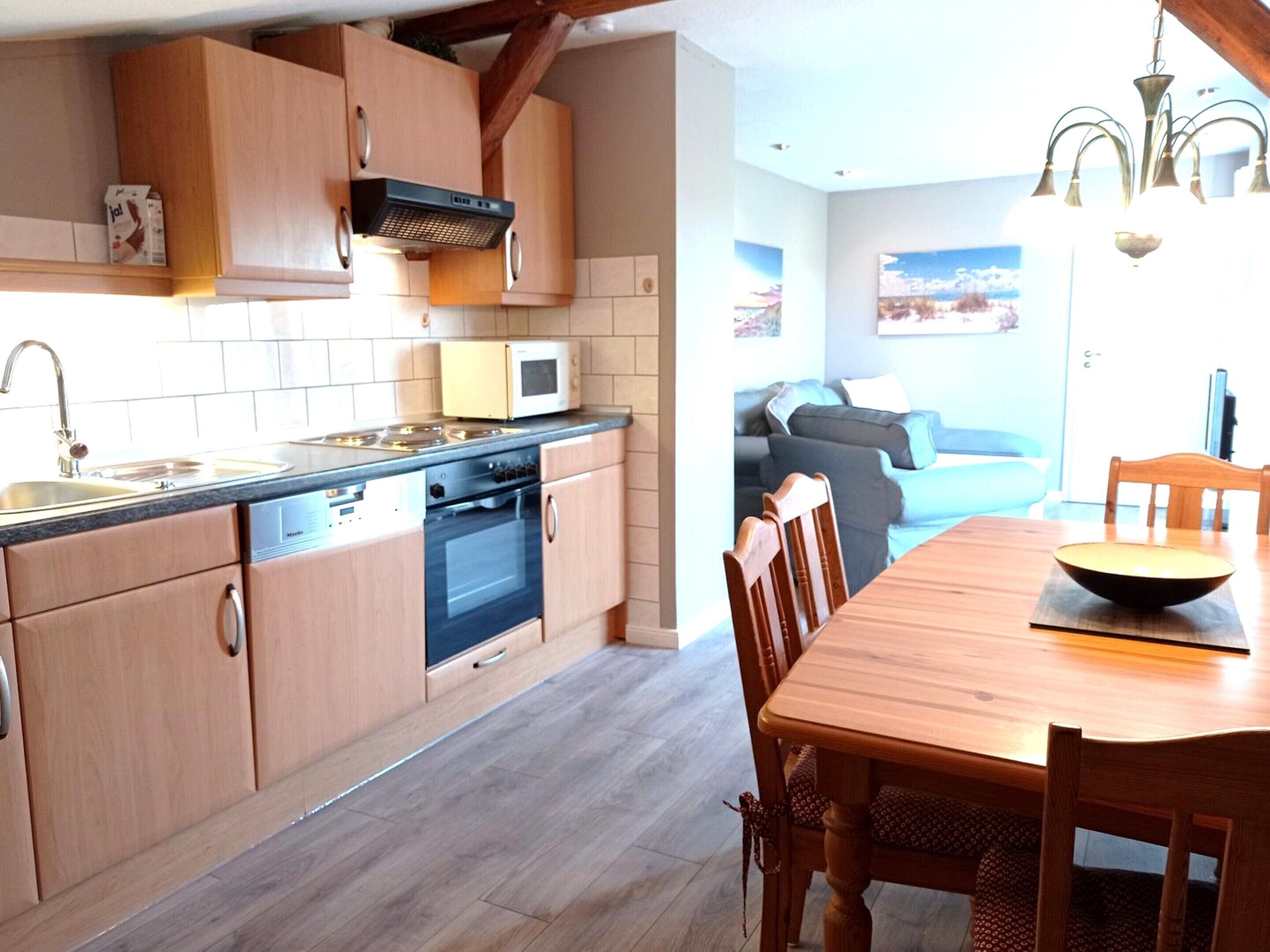 Una cocina con armarios de madera, estufa, microondas y comedor con mesa y sillas.