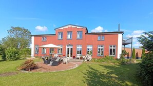 A two-story building with a patio area featuring outdoor furniture and a covered seating area. - Moderne Ferienwohnung mit Meerblick (Fehmarn)
