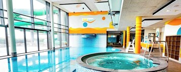An indoor swimming pool with clear glass walls, a hot tub, and a colorful mural on the wall.