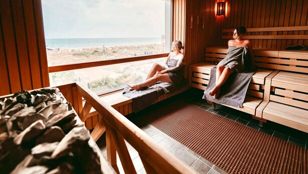 A sauna with wooden benches and a large window overlooking a beach. - Moderne Ferienwohnung mit Meerblick (Fehmarn)