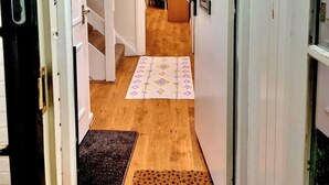 A hallway with a wooden floor, a patterned rug, a doormat, and a door with a security camera. - 4 bedroom duplex in central London with private entrance (London)